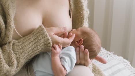 Close-Up-An-Unrecognizable-Mother-Breastfeeding-Her-Newborn-Baby-While-Sitting-On-The-Bed-At-Home