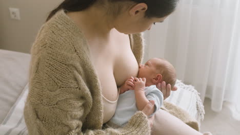 Liebevolle-Junge-Mutter,-Die-Ihr-Neugeborenes-Baby-Stillt,-Während-Sie-Zu-Hause-Auf-Dem-Bett-Sitzt-1