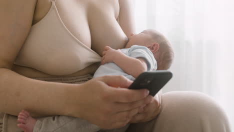 Unrecognizable-Mother-Breastfeeding-Her-Newborn-Baby-And-Using-Mobile-Phone-While-Sitting-On-The-Bed-At-Home-1