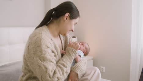 Brunette-Woman-Sitting-On-The-Bed-Holding-Her-Baby-And-Caressing-Him