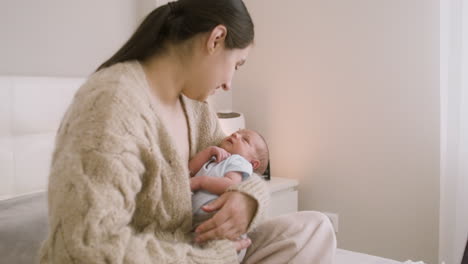 Brunette-Woman-Sitting-On-The-Bed-Holding-Her-Baby-And-Talking-To-Him