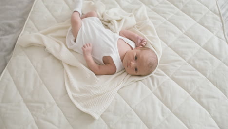 Draufsicht-Auf-Ein-Baby-Im-Weißen-Body,-Das-Auf-Dem-Bett-Liegt-Und-Seine-Beine-Und-Arme-Bewegt