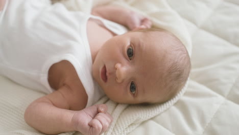 Nahaufnahme-Eines-Babys-Im-Weißen-Body,-Das-Auf-Dem-Bett-Liegt-Und-Seine-Arme-Bewegt