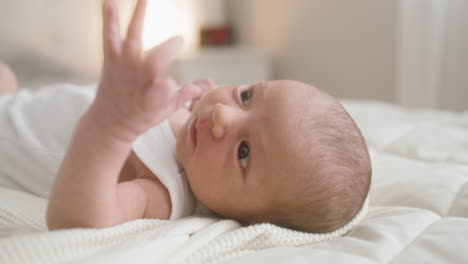Close-Up-View-Of-A-Baby-In-White-Bodysuit-Lying-On-Bed-Moving-His-Arms-1