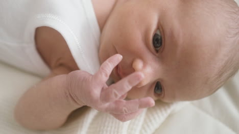 Close-Up-View-Of-A-Baby-In-White-Bodysuit-Lying-On-Bed-Thumbsucking-And-Moving-His-Arms