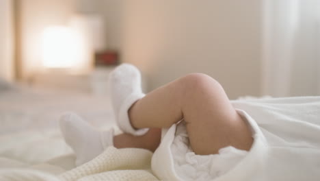 Close-Up-View-Of-A-Baby's-Legs-Lying-On-The-Bed-In-White-Booties