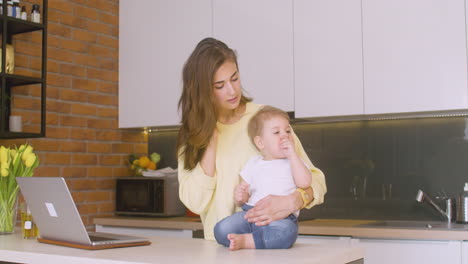 Woman-Holding-Her-Baby-On-The-Kitchen-Counter-While-Talking-On-The-Phone