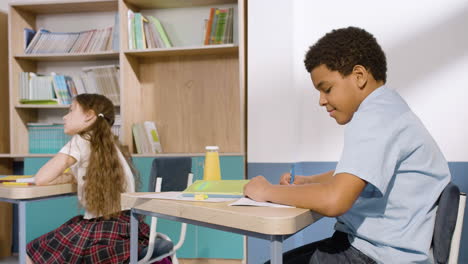 Kleines-Mädchen-Und-Amerikanischer-Junge-Sitzen-Am-Schreibtisch-Und-Machen-Sich-Während-Des-Schulunterrichts-Notizen