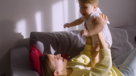 Woman-Lying-On-The-Sofa-At-Home-While-Playing-With-Her-Baby