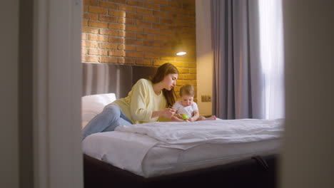 Distant-View-Of-Woman-And-Her-Baby-Sitting-On-The-Bed-At-Home