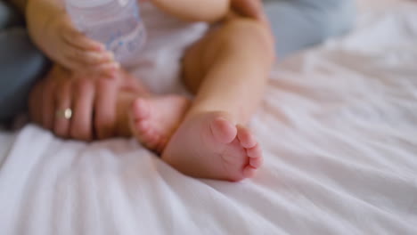 The-Camera-Focuses-On-A-Babyâ€šÃ„Ã´s-Feet-While-The-Baby-Is-Playing-With-Feeding-Bottle-And-His-Mother-Caressing-His-Legs-On-The-Bed