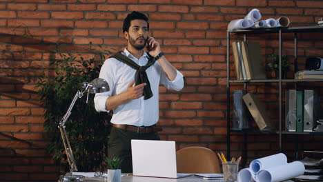 Joven-Hombre-De-Negocios-árabe-Caminando-En-La-Moderna-Sala-De-Oficinas,-Hablando-Por-Teléfono-Y-Gesticulando