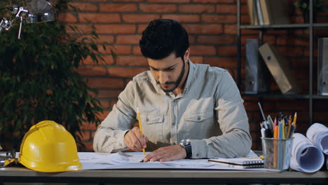 Junger-Arabischer-Architekt,-Der-Am-Schreibtisch-Im-Büro-Sitzt-Und-An-Den-Neuen-Projektzeichnungen-Arbeitet