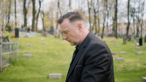 Close-Up-View-Of-Man-In-Black-Suit-Kneeling-In-Front-Of-A-Grave