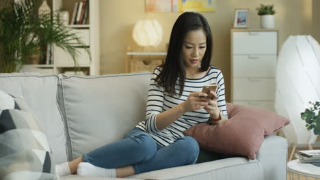 Young-Charming-Woman-Sitting-On-The-Couch-At-Home-With-A-Smartphone-In-Hands-And-Shopping-Online-With-A-Credit-Card