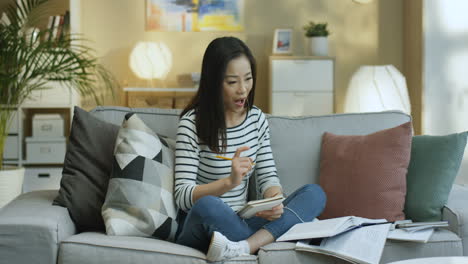 Young-Woman-In-Striped-Shirt-And-Wearing-Headphone-Studying-With-Textbooks-And-Taking-Notes-On-Notebook