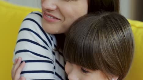 Close-Up-View-Of-Mother-And-Small-Daughter-Sitting-On-Yellow-Couch-And-Then-Hugging-Cheerfully