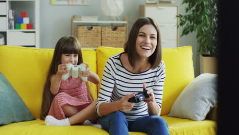 Fröhliche-Junge-Mutter-Und-Tochter-Spielen-Videospiel-Mit-Joystick,-Während-Sie-Auf-Der-Couch-Im-Wohnzimmer-Sitzen
