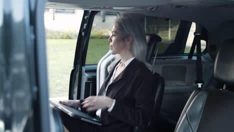 Gray-Haired-Woman-With-Laptop-In-Official-Suit-Getting-Into-Car