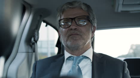 Senior-Bearded-Businessman-With-Suit-And-Glasses,-Sitting-In-Backseat-Of-Moving-Car