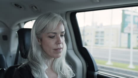 Gray-Haired-Woman-Sitting-In-Backseat-Of-Moving-Car