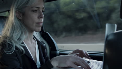 Gray-Haired-Woman-In-Suit-Typing-On-Laptop-In-Car
