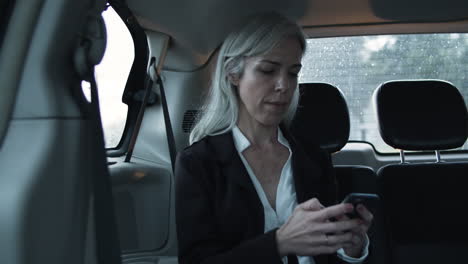 Focused-Woman-Sitting-In-Moving-Car,-Writing-Message-On-Phone