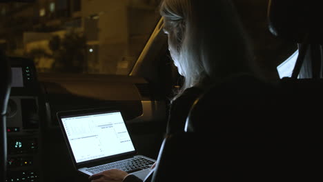 Back-View-Of-Businesswoman-Using-Laptop-In-Car-At-Night