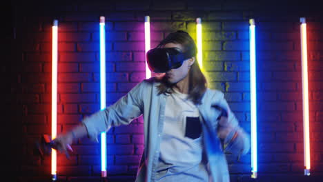 Young-Man-With-Long-Hair-In-Vr-Glasses-Playing-A-Game-In-A-Room-With-Colorful-Neon-Lamps-On-The-Wall