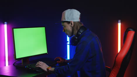 Young-Man-Playing-On-The-Computer-With-Chroma-Key-Screen,-Then-Looks-At-The-Camera-And-Smiles