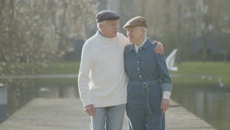 Happy-Elderly-Couple-Walking-Along-Wooden-Pier-In-City-Park