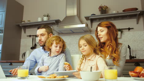 Fröhliche-Familie-Beim-Frühstück,-Während-Sie-Einen-Laptop-Und-Ein-Tablet-Benutzen
