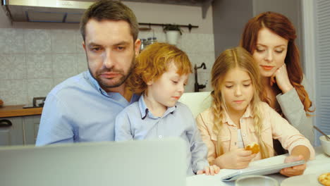 Parents-And-Kids-Eating-Cookies-In-The-Kitchen-While-They-Look-At-Something-On-A-Laptop
