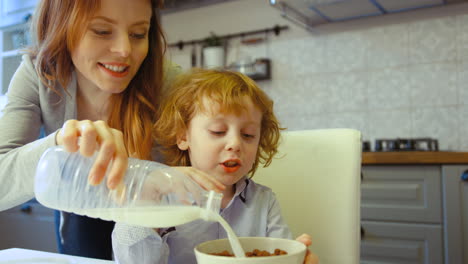 Beautiful-Young-Woman-With-Red-Hair-Pouring-Milk-In-Plate-With-Cereal-For-Her-Son-In-The-Kitchen