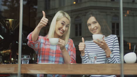 Portrait-Shot-Of-A-Blonde-And-Brunette-Girls-Spending-Their-Morning-Together-And-Having-A-Conversation-While-Drinking-Coffee-In-A-Cafe