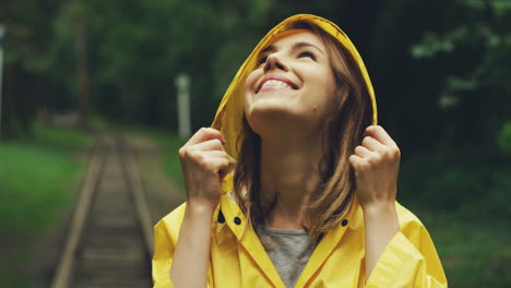 Close-Up-Of-A-Happy-Girl-In-A-Yellow-Raincoat-Smiling-Joyfully-And-Looking-Up-In-The-Sky