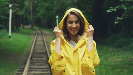 Portrait-Of-An-Woman-In-A-Yellow-Rainproof-Coat-Standing-In-Front-Of-The-Camera-And-Laughing-In-The-Forest