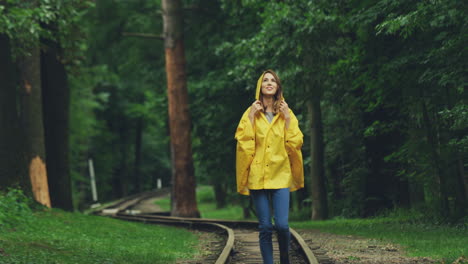 Fröhliche-Junge-Frau-In-Einem-Gelben-Regenmantel,-Die-Während-Des-Regensturms-Glücklich-Auf-Der-Alten-Eisenbahn-Läuft