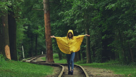 Charmantes-Mädchen-In-Einem-Gelben-Regenmantel,-Der-Glücklich-Auf-Der-Alten-Eisenbahn-Im-Wald-Läuft-Und-Geht