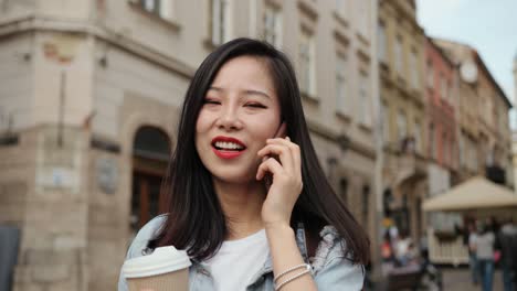 Close-Up-Of-The-Cheerful-Young-Girl-Speaking-On-The-Phone-And-Laughing-While-Walking-The-City-Center-With-A-Coffee-To-Go