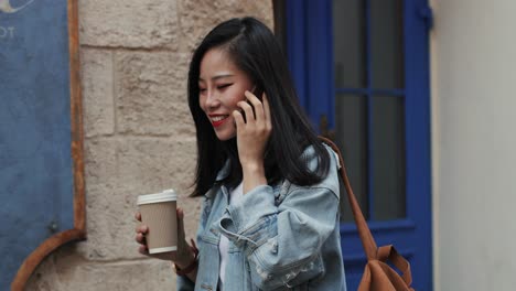 Cheerful-Stylish-Pretty-Woman-Walking-The-Nice-Town-Street,-Carrying-A-Coffee-To-Go-In-Hand-And-Speaking-On-The-Mobile-Phone