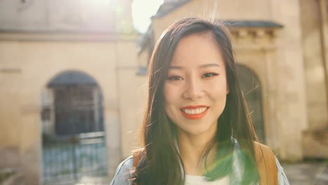 Portrait-Of-The-Beautiful-Young-Woman-With-Red-Lips-Turning-Her-Face-To-The-Camera-And-Smiling-Happily-While-Having-Sightseeing-Roung-The-City-On-A-Sunny-Day