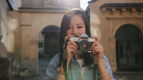 Portrait-Shot-Of-The-Pretty-Young-Female-Photograph-Taking-A-Photo-With-Professional-Camera-And-Then-Smiling-To-The-Camera-Among-Historical-Buildings