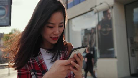 Close-Up-Of-The-Young-Brunette-Smiled-Woman-Tapping-And-Typing-A-Message-On-The-Smartphone-In-The-City-Center