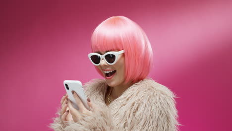 Mujer-Atractiva-Con-Gafas-De-Sol-Y-Una-Peluca-Rosa-Tocando-Y-Enviando-Mensajes-De-Texto-En-El-Teléfono-Inteligente