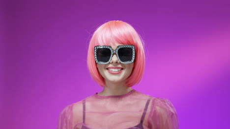 Porträt-Einer-Stilvollen-Frau,-Die-Eine-Rosa-Perücke-Und-Eine-Glamouröse-Sonnenbrille-Trägt,-In-Die-Kamera-Lächelt-Und-Küsse-Bläst