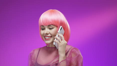 Cheerful-Woman-Wearing-A-Pink-Wig-And-Stylish-Outfit-Talking-On-Mobile-Phone-And-Smiling