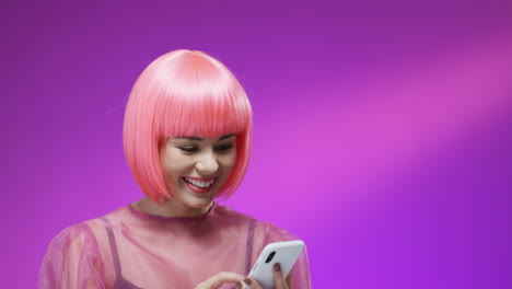 Close-Up-Of-Pretty-Woman-Wearing-A-Stylish-Pink-Wig-Smiling-Cheerfully-With-A-Smartphone-In-Her-Hands-1