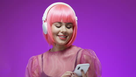 Schöne-Frau,-Die-Eine-Rosa-Perücke-Und-Große-Kopfhörer-Mit-Smartphone-In-Den-Händen-Trägt,-Tanzt-Und-Lacht