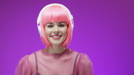 Beautiful-Woman-Wearing-A-Pink-Wig-And-Headphones,-Listening-To-Music-And-Smiling-To-Camera
